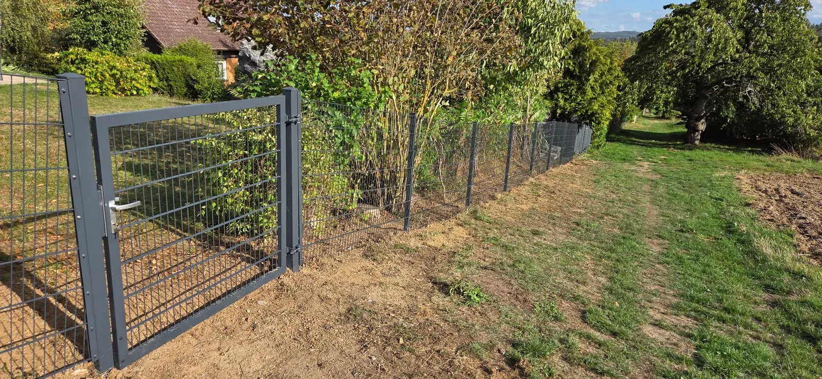 Doppelstabmattenzaun 1,43 m in Anthrazit mit Gartentor hinter einem Wohnhaus in Usingen, Zaunverlauf in Hanglage zum Feldweg